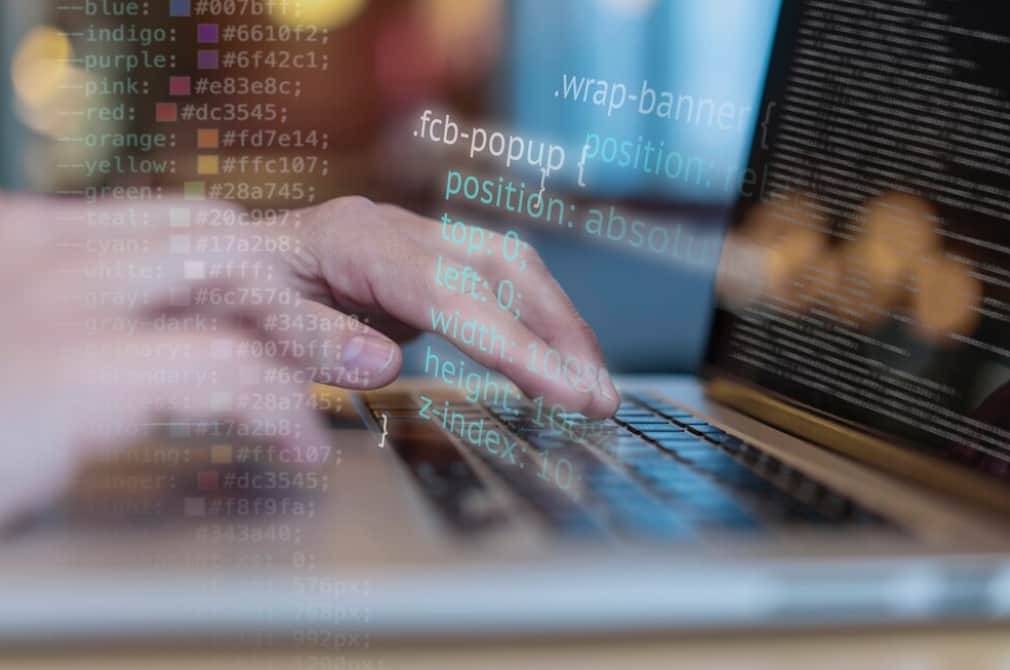 Close-up of hands coding with colorful syntax highlighting on a laptop screen