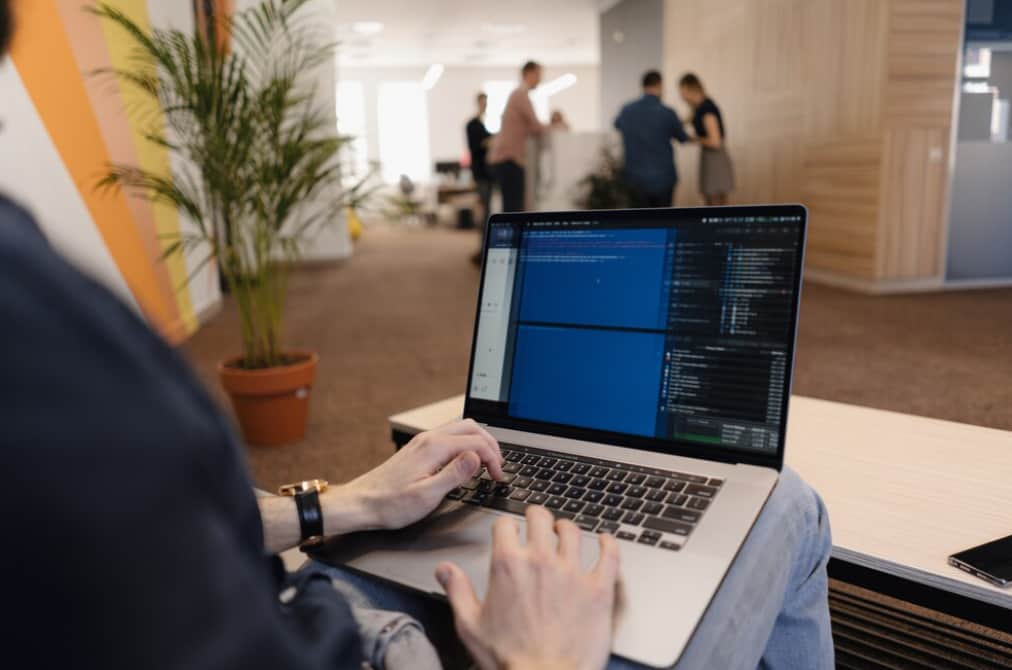 a person with a laptop sitting near the table in the office, people on a blurred background