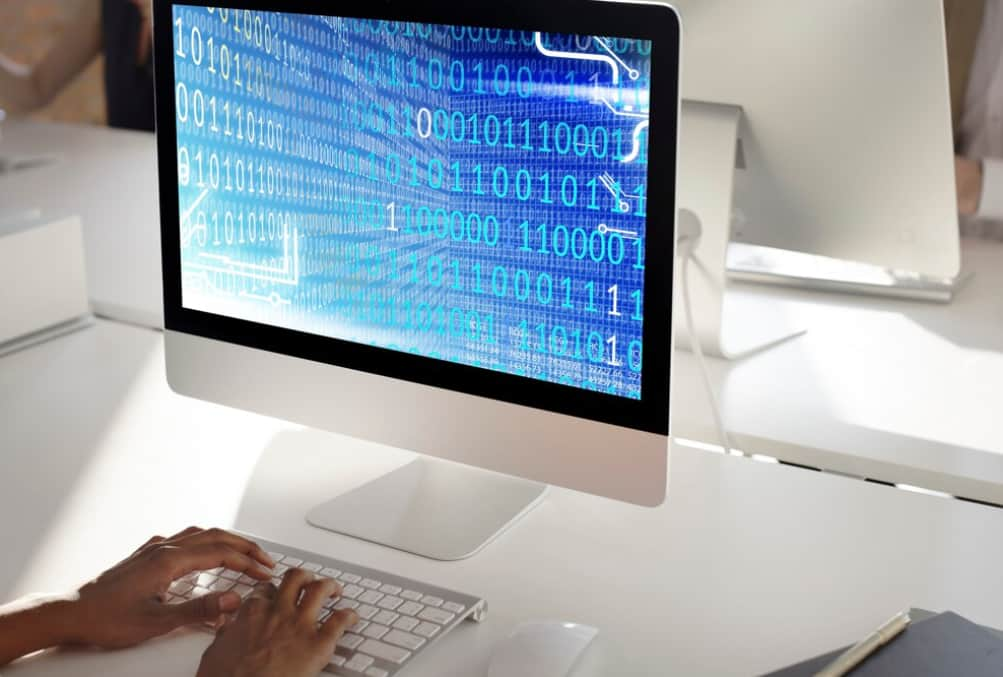 hands typing on the keyboard, binary code on blue background on the computer screen